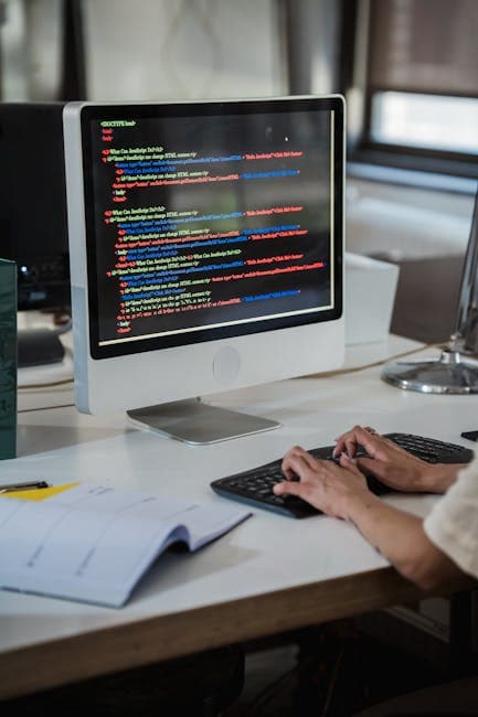 Close-up of a person typing code on a computer in an office setting.