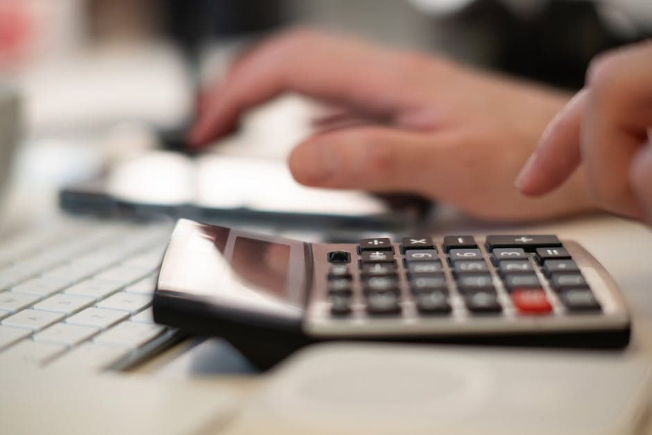 Close-up of hands using a calculator and keyboard in a financial setting, indoors.