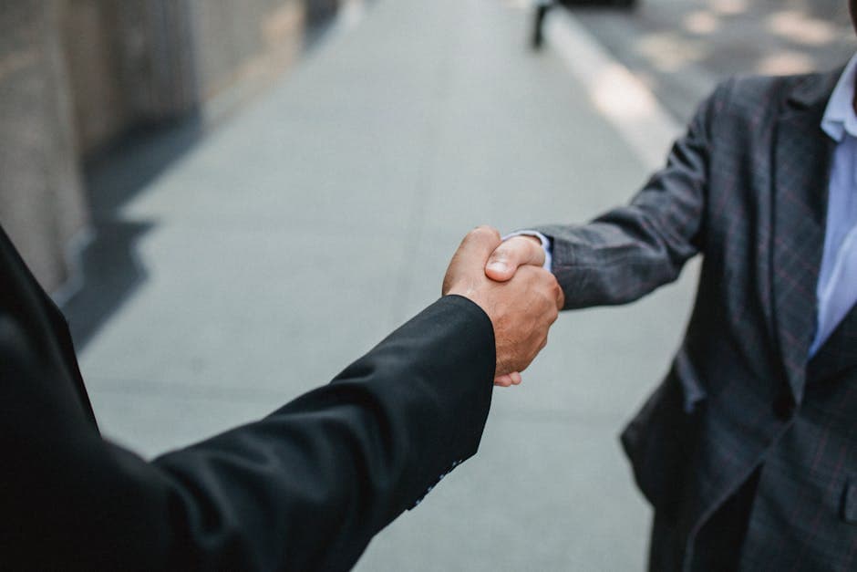 Close-up of two businessmen shaking hands outside, symbolizing partnership and agreement.