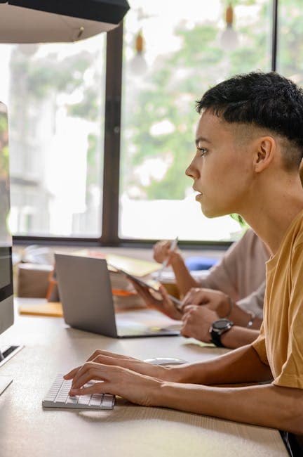 A young adult working at a desk with a computer in a modern office environment.