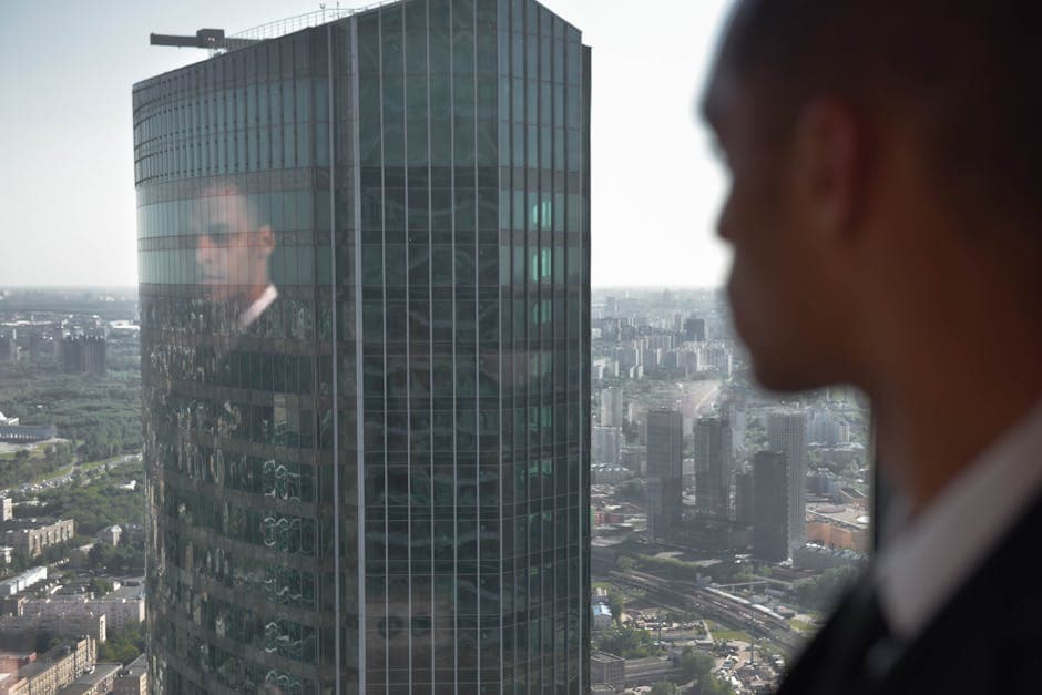 Businessman gazing out at urban skyline, cityscape reflected in glass skyscraper.