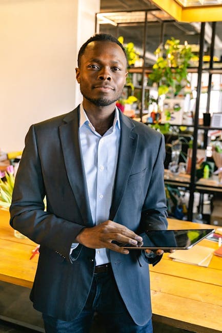 Young professional in a suit holds a tablet in a modern office, embodying business confidence and technology use.