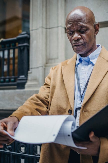 From below of pensive black entrepreneur in trendy outfit standing on street and reading documents in folder in daylight