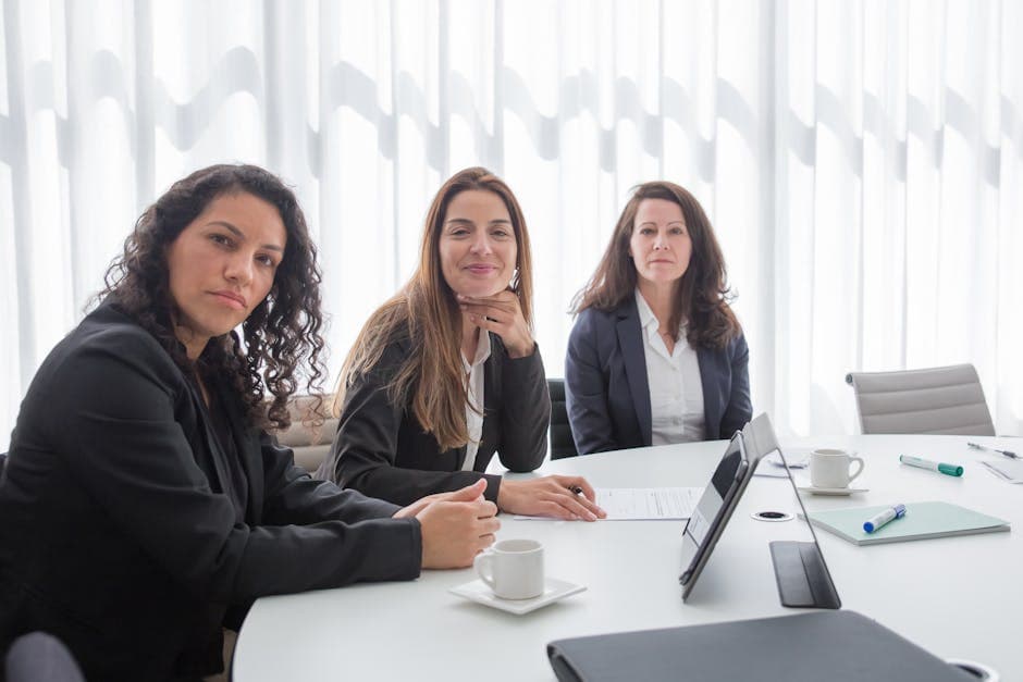 Three businesswomen in a modern office setting, engaged in discussion at a conference table.