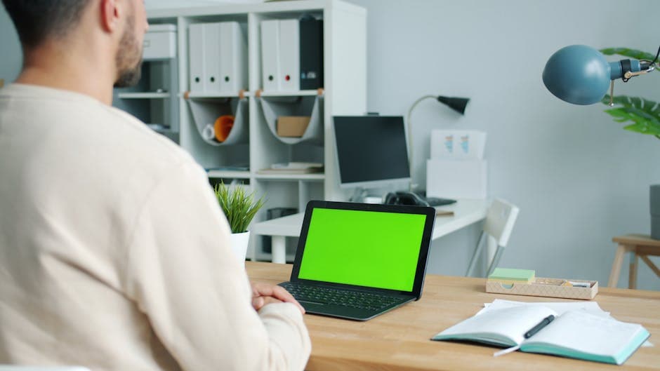 Home office setup with a man using a laptop with green screen.