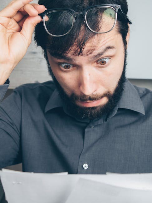 A man with eyeglasses looks surprised while reading. His expression shows shock and disbelief.