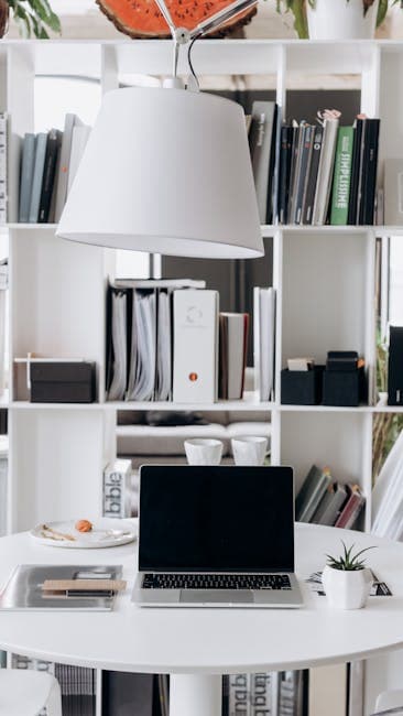 Elegant minimalist home office setup featuring a laptop on a white desk with stylish shelves in the background.