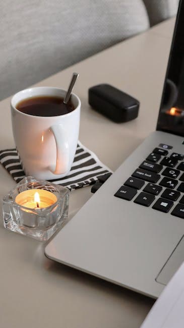 A relaxing workspace setup featuring a cup of tea, candle, and laptop for productivity.