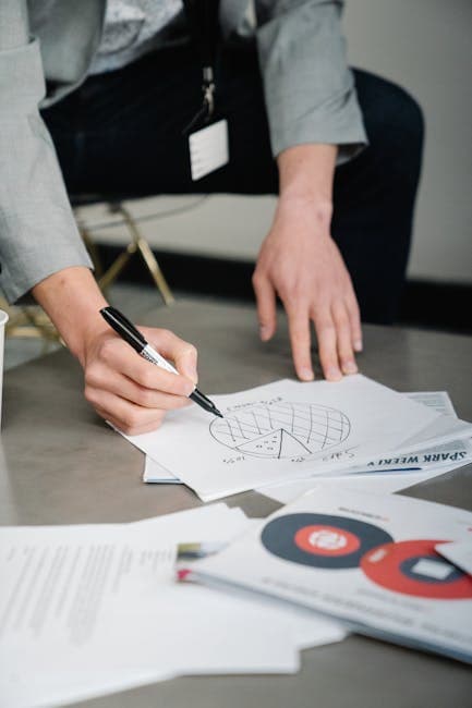 Close-up of a professional analyzing business charts on paper with a marker.
