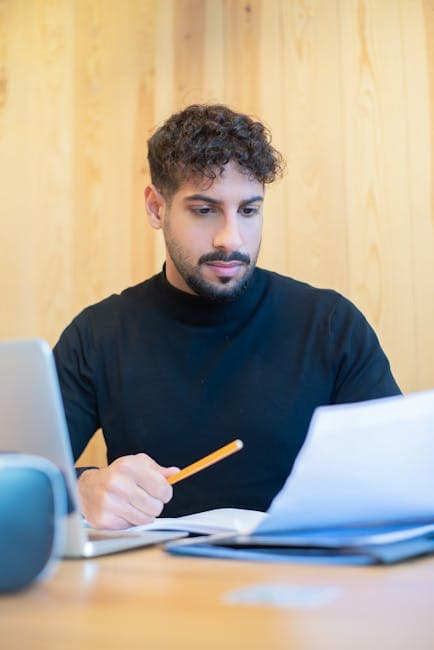 Focused young man reviewing documents at a desk in a modern office setting.