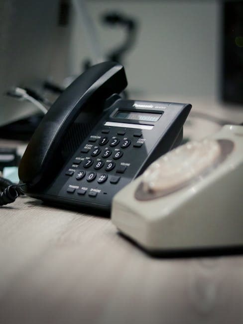 A close-up of a classic rotary and modern landline phone on a desk.