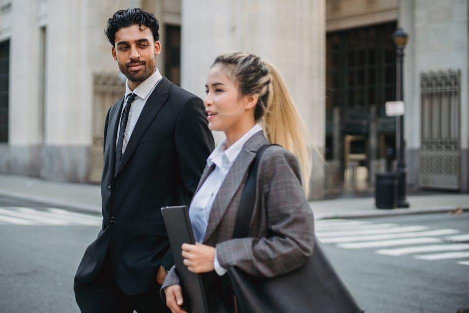 Two business professionals in formal attire walking on a city street, engaged in conversation.