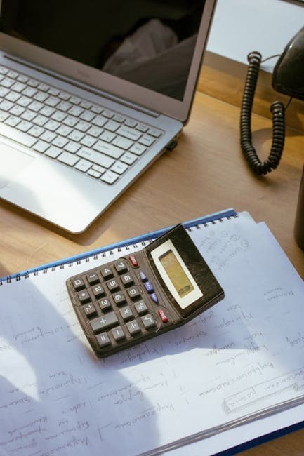 Cozy office workspace with a calculator, laptop, and notes on a wooden desk.