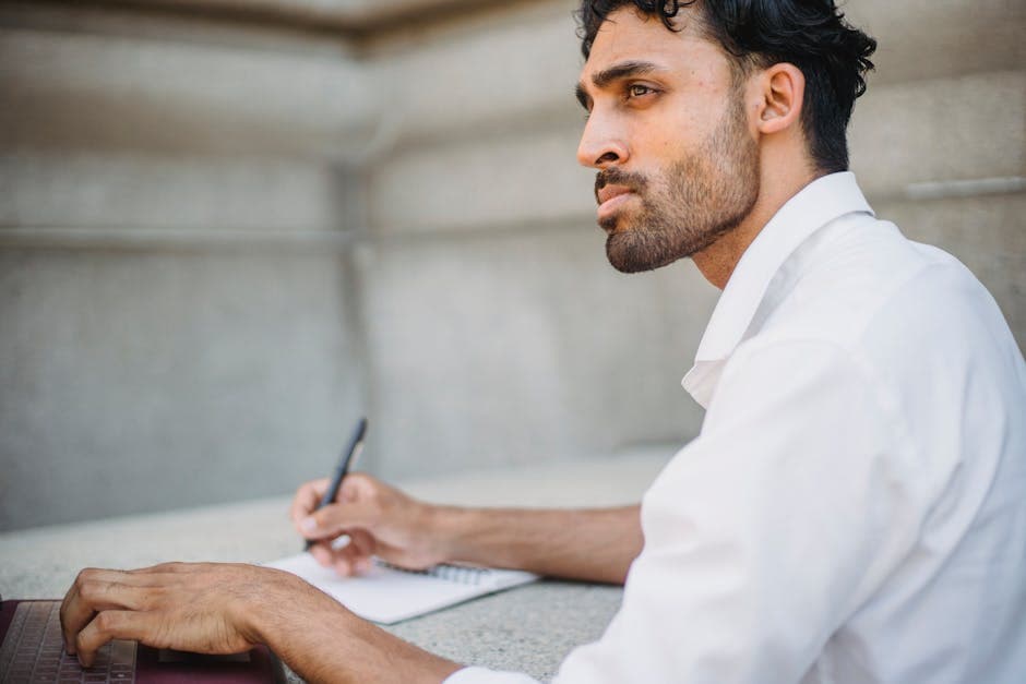 Focused young businessman taking notes on a notepad while working outdoors.
