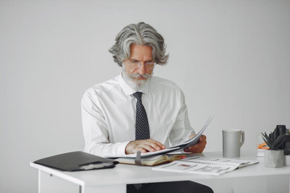 An elderly businessman reviewing documents at his desk in a modern office setting.